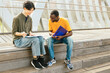 © ADDICTIVE STOCK - Two Friends Studying Together Outdoors on Wooden Steps