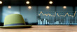 © Adisak - Green bowler hat on wooden desk with business charts in background