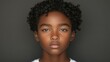 © imagineRbc - A young boy with curly hair stands upfront, looking straight at the camera with an expression of calm confidence. His skin has a warm tone, contrasting with the dark backdrop