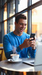 © Inspire Shots Hub - A young man in a casual blue sweater smiling while holding a smartphone in a coffee shop, symbolizing happiness, success, and modern lifestyle.