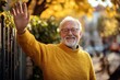 © Yevhen - Joyful Senior Man in Yellow Pullover Greeting Neighbour with a Wave at the Fence