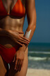 © Mirrorstudio - Young female applying sunscreen on a sunny beach in red bikini. Skin care, sun protection