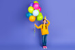 © deagreez - Adorable preteen girl in casual yellow sweatshirt with colorful balloons, celebrating with happy expression over purple background