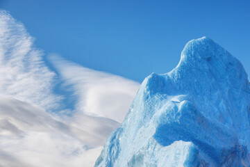 Wall Mural - detail of a blue iceberg against blue sky and cloud background. kjerulf fjord, northeast greenland n