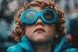 © Milos - Young child wearing bright goggles looking up while enjoying a rainy day outdoors in an urban setting