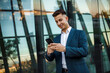 © Marko - Businessman Using Smartphone Outside Modern Office Building