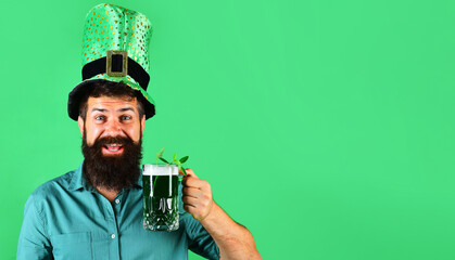 Wall Mural - Patrick Day pub party. Happy bearded man in green shirt and top hat drinking green beer. Irish tradition. Bearded man in leprechaun hat holds mug of green beer with clover. Copy space for advertising.