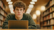 © Bonsales - Young european man sitting at desk in public library, using laptop for online gambling, looking up with serious expression