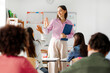 © Home-stock - Friendly young European female teacher giving high five to pupil, standing near her desk and smiling. Education, teaching, learning at private school concept