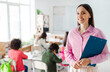 © Home-stock - Positive young European teacher standing in classroom with group of pupils on background during lesson. Teaching, education concept