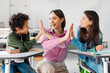 © Home-stock - Happy friendly female teacher, schoolgirl and Latin schoolboy cheering, giving high five to each other, enjoying teamwork and project result
