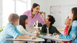 © Home-stock - Cheerful teacher talking to kids, children sitting at desks in classroom and listening their teacher with interest, panorama