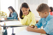 © Home-stock - Positive schoolgirl sitting at table near boy classmate and helping with task, writing in his copybook, enjoying learning process in school