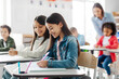 © Home-stock - Focus on happy school girls sitting at desk, doing tasks and writing in copybooks, one girl glances at her friend's test, studying at school