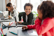 © Home-stock - Latin boy chatting with girl during lesson, sitting in school classroom with laptops on desk. Classmates study in classroom. Modern technology education