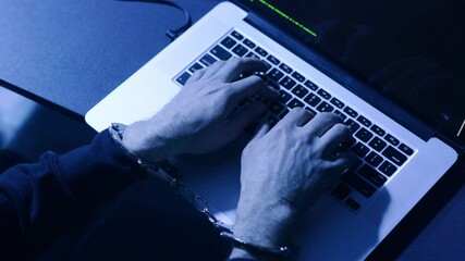 Hands are diligently typing on a laptop which displays a coding screen in a dark environment