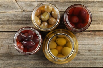 Wall Mural - Pickled olives in glass jars on wooden table, flat lay