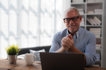 Wall Mural - Happy businessman working from home, using laptop computer at desk, smiling mature professional having online meeting or video conference call, enjoying remote work