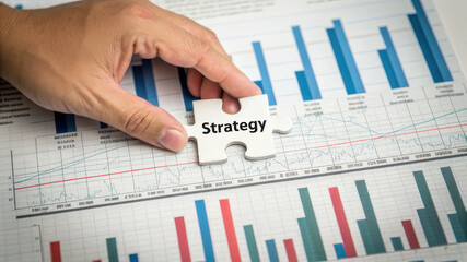 Poster - Hand placing puzzle piece labeled Strategy on financial report, symbolizing planning and analysis. , Recession concept