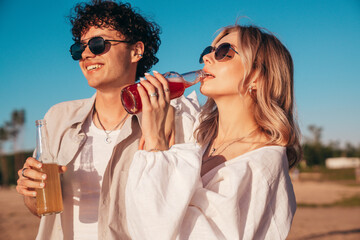 Sticker - Young stylish friends posing at the seaside. Fashion man and cute female dressed in casual summer clothes. Smiling models having fun. Cheerful women and guy outdoors, Hold and drink lemonade