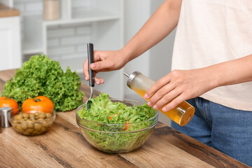 Wall Mural - Woman adding olive oil into bowl with tasty salad at table in kitchen