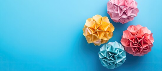 Poster - Colorful origami paper flowers in pastel shades of yellow, pink, and blue arranged on a soft blue background with ample negative space.