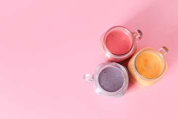 Wall Mural - Mason jars of different fresh smoothie on pink background