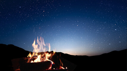 Wall Mural - a bonfire burns at night against the background of mountains and sea with bright stars...