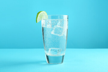 Canvas Print - Soda water with lime and ice cubes in glass on light blue background