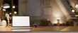 © bongkarn - A white screen laptop on the wooden table in lamp light, with the blurred background of dim light room.