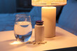 © Pixel-Shot - Melatonin pills with glass of water and glowing lamp on table in bedroom at night, closeup
