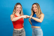 Two young women fist bumping celebrating success on blue background