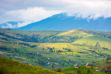 Wall Mural - mountainous rural landscape in spring. trees and agricultural fields on hills rolling in to the distant valley. ridge beneath a overcast sky in dappled light. beautiful provincial scenery for vacation