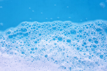 Wall Mural - Foam on blue background. Liquid soap bubbles