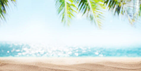 Poster - A tranquil seaside landscape with soft-focus palm leaves in the foreground and a golden sandy beach under the warm sunlight