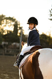A young girl rider in a helmet and equestrian boots sits on her beloved horse at the stable, enjoying a peaceful horseback ride.