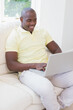 © WavebreakMediaMicro - African American man using laptop on couch, smiling and working from home