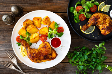 Wall Mural - Oven roasted chicken thigh with fried potatoes and fresh salad on wooden table	