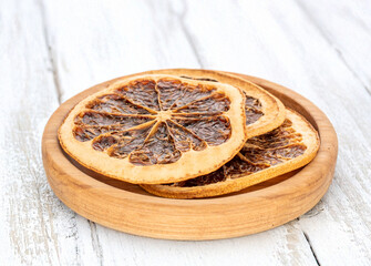 Wall Mural - Several dried grapefruit slices on a wooden plate on a wooden table, close-up.