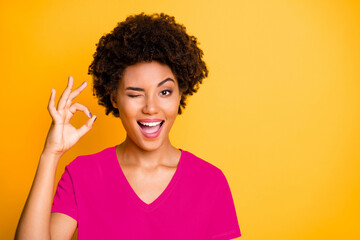 Wall Mural - Copyspace photo of cheerful blinking curly wavy trendy woman showing you ok sign winking wearing orange t-shirt isolated over yellow bright color background