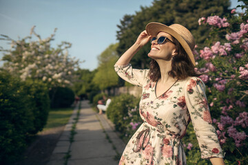 stylish young woman wearing a floral dress, sunglasses, and a straw hat, enjoying the warm spring su