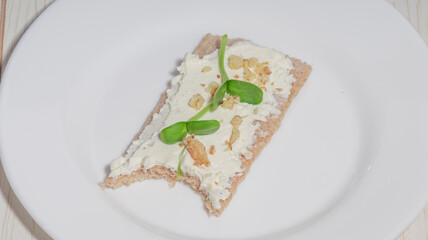 Close-up of a crispbread with cream cheese, walnuts, and microgreens on a plate.