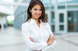 © Minerva Studio - Smiling businesswoman standing with arms crossed in front of office building