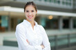 © Minerva Studio - Smiling businesswoman standing with arms crossed in front of modern office building