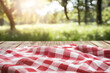 © Jannik - Empty wooden table with a red and white checkered kitchen towel over a blurred nature background