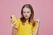© SHOTPRIME STUDIO - Young girl with a yellow smartphone, showing a confused expression against a pink background, representing modern communication and digital age