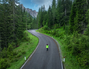 Wall Mural - woman walking on a winding mountain road in lush green forest on summer rainy day. dolomites, italy.