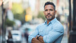 © Oppilamani - A Confident Latino Man in His Mid-40s Posing with Arms Crossed on a Bustling City Street, Exuding Determination and Self-Assurance Amidst an Urban Landscape