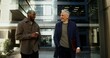© m-art - An African-American man with a cup of coffee and a gray-haired Caucasian man with a laptop are smiling while talking in the business center of the city on a sunny day. Video in 4k, red komodo