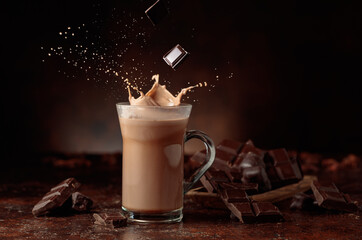 Wall Mural - Pieces of bitter chocolate fall in glass mug with cocoa drink.